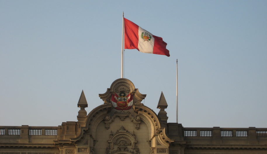 The national flag of Peru waving on a flagpole on top of a Spanish-colonial style building during day time.