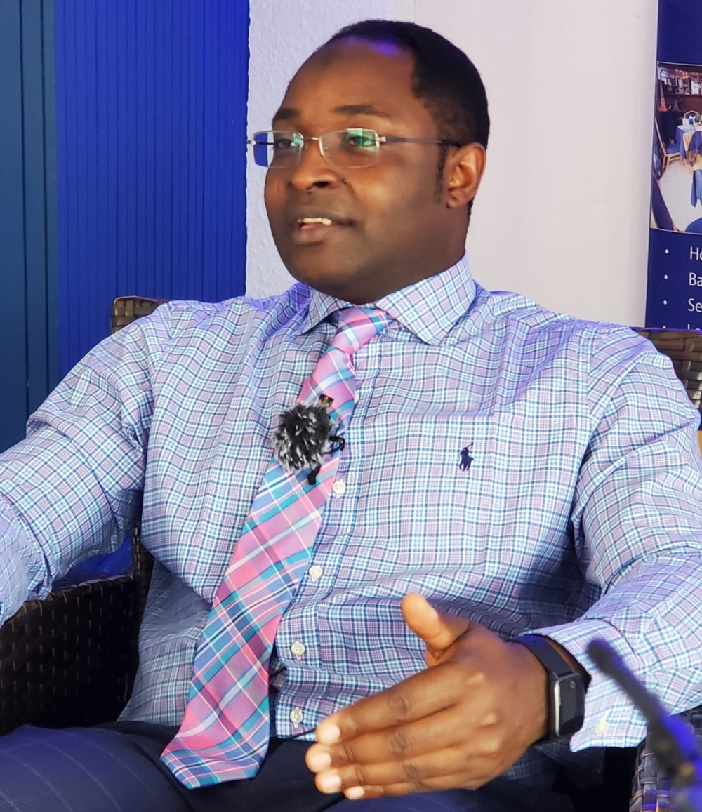 Abdul Karim Ali is Cameroonian activist. In this picture, he is wearing a shirt with tie and is seated in a chair with a blue and white back drop.