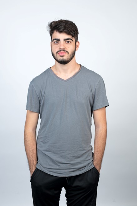 Yuval Dag wearing a grey t-shirt and black pants standing in front of a white background.