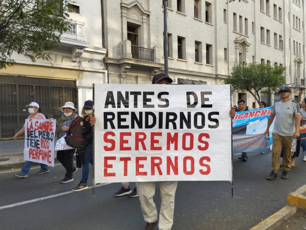 A protester marching on a city streets hold a sign with words in Spanish that translate to "before we surrenderwe will be eternal."