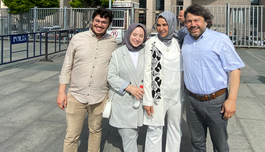 Four people — two men on the outside and two Hijab-wearing women on the inside — smile for the camera outside a police station.
