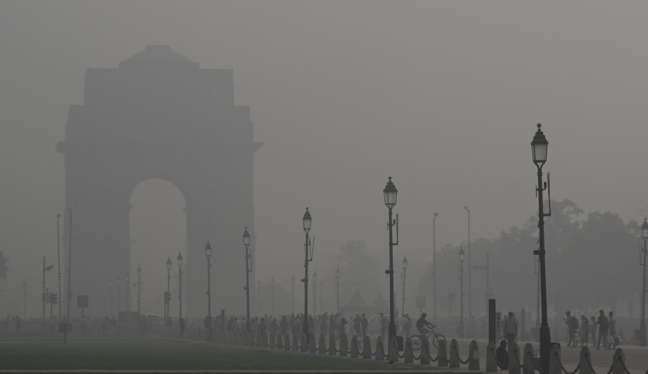 A thick layer of grey smog blankets an arch and street lamps on a street being used by cyclists and pedestrians