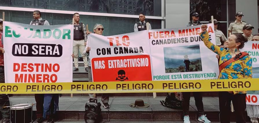 protest outside Canada's Embassy in Ecuador with signs that say "Danger" and "FTA with Canada = more poisonous extractivism"